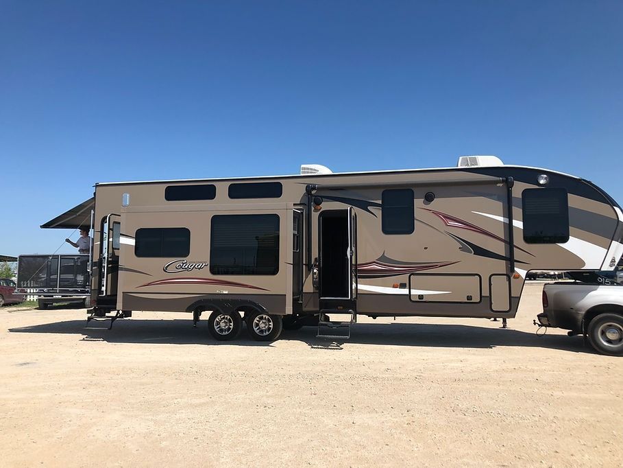 A rv is parked in a gravel lot next to a truck.