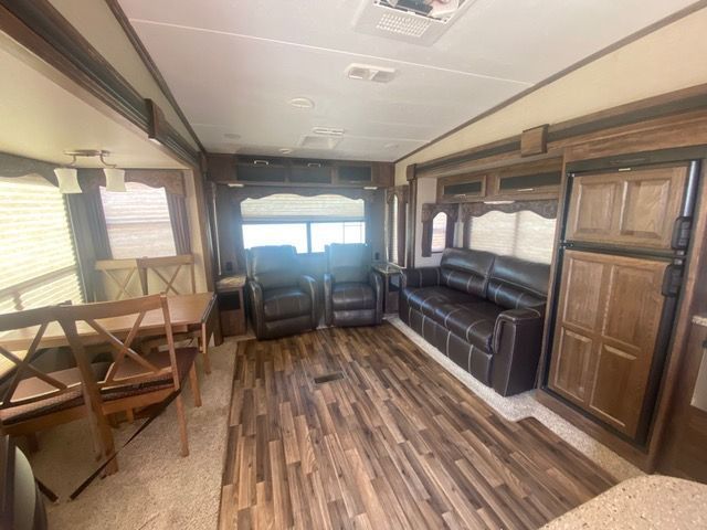 A living room in a trailer with a couch , chairs , a table and a refrigerator.