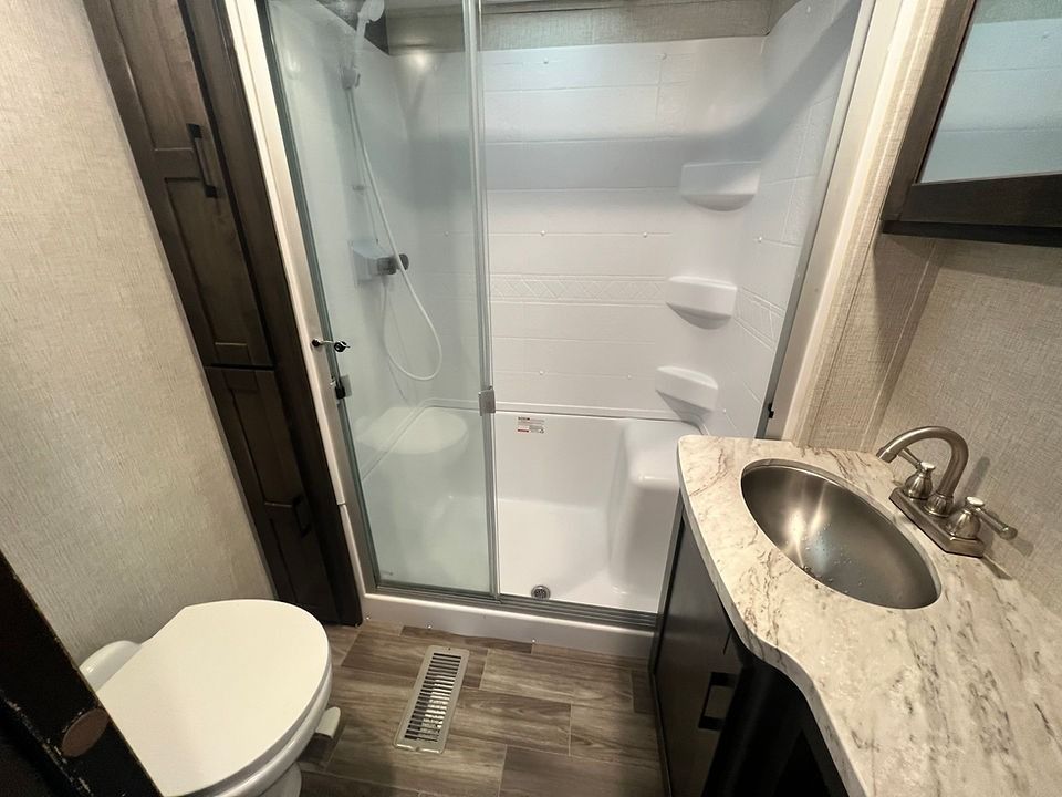 A bathroom with a toilet , sink and shower.