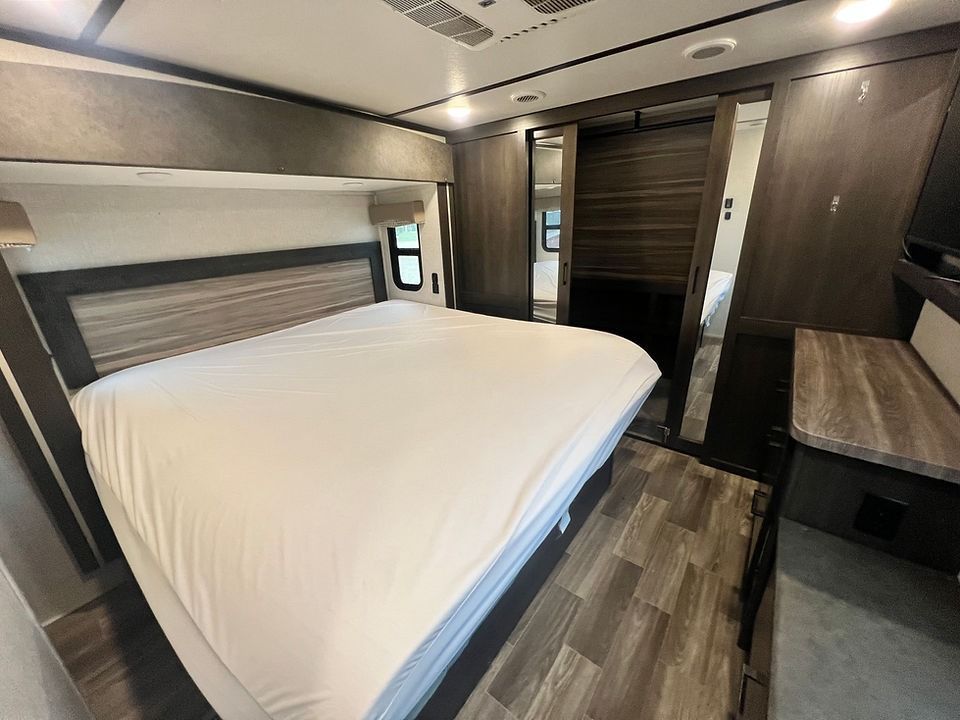 A bedroom in a rv with a king size bed and a desk.