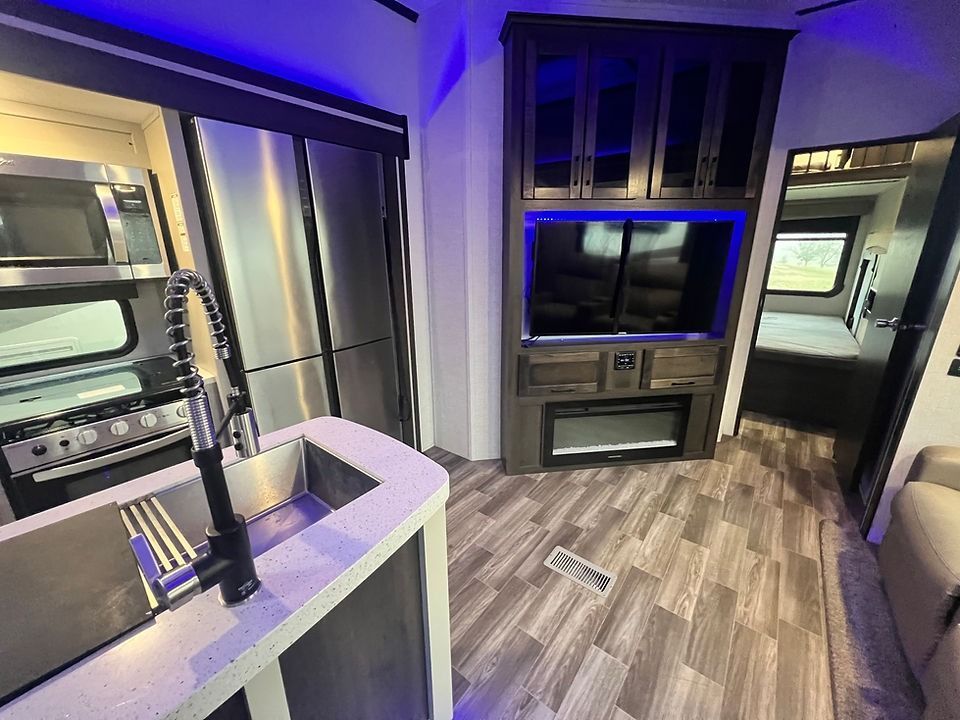 A kitchen in a rv with a sink , refrigerator , microwave and television.