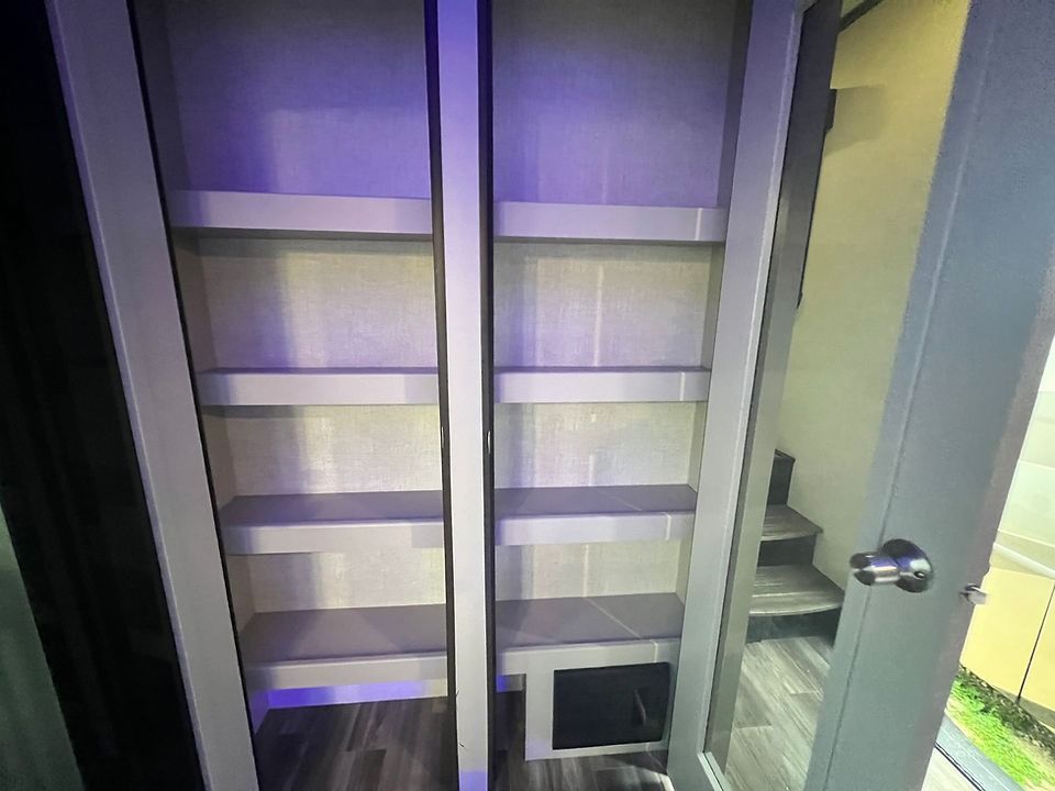 A closet with purple lights on the shelves and stairs in the background.
