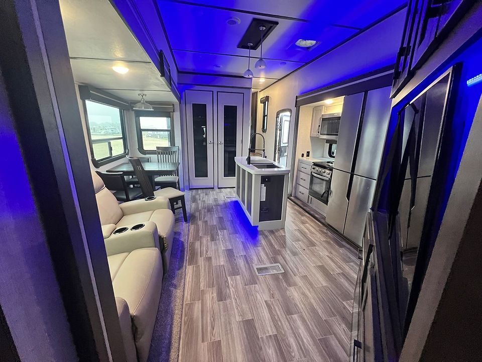 A living room and kitchen in a rv with blue lights.