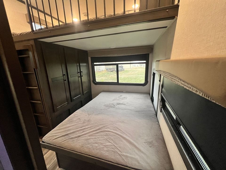 A bed in a rv with a bunk bed underneath it.