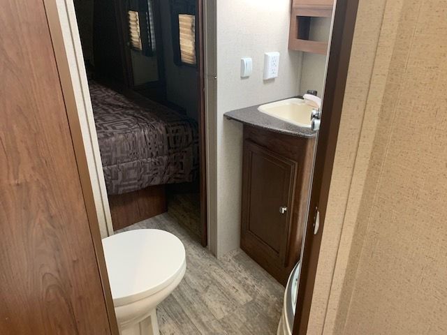 A bathroom in a trailer with a toilet , sink and bed.