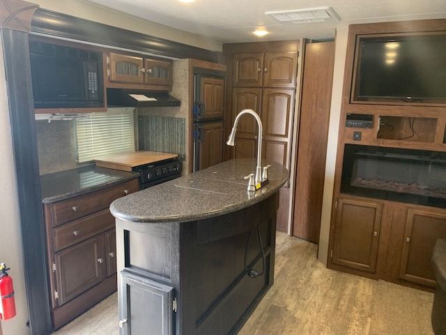 A kitchen with a large island , stove , refrigerator and television.