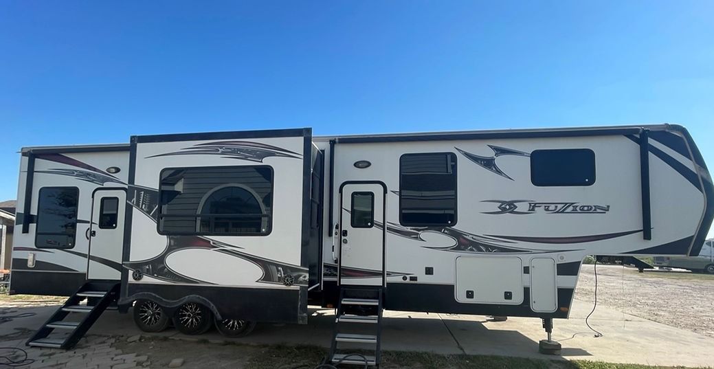 A white and black rv is parked in a dirt field.