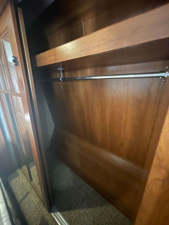A wooden closet with a metal railing and a mirror.