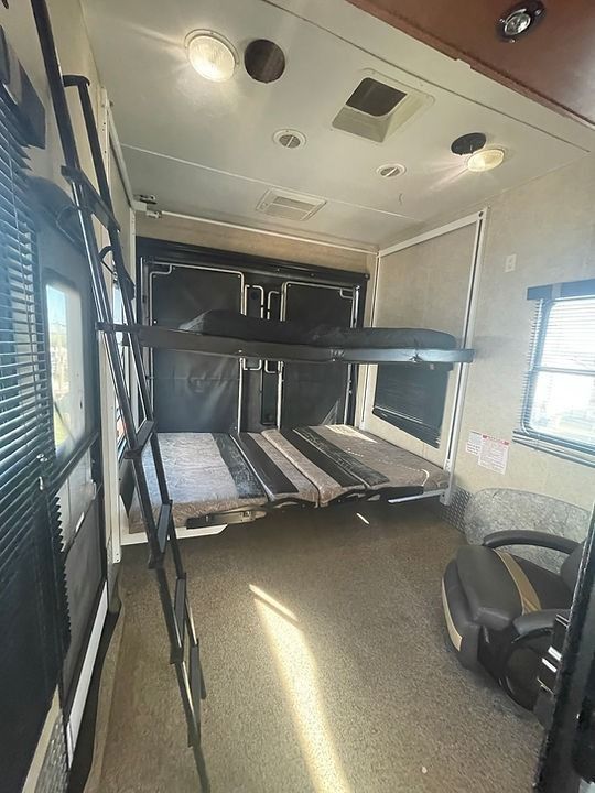 A room in a rv with bunk beds and a chair.