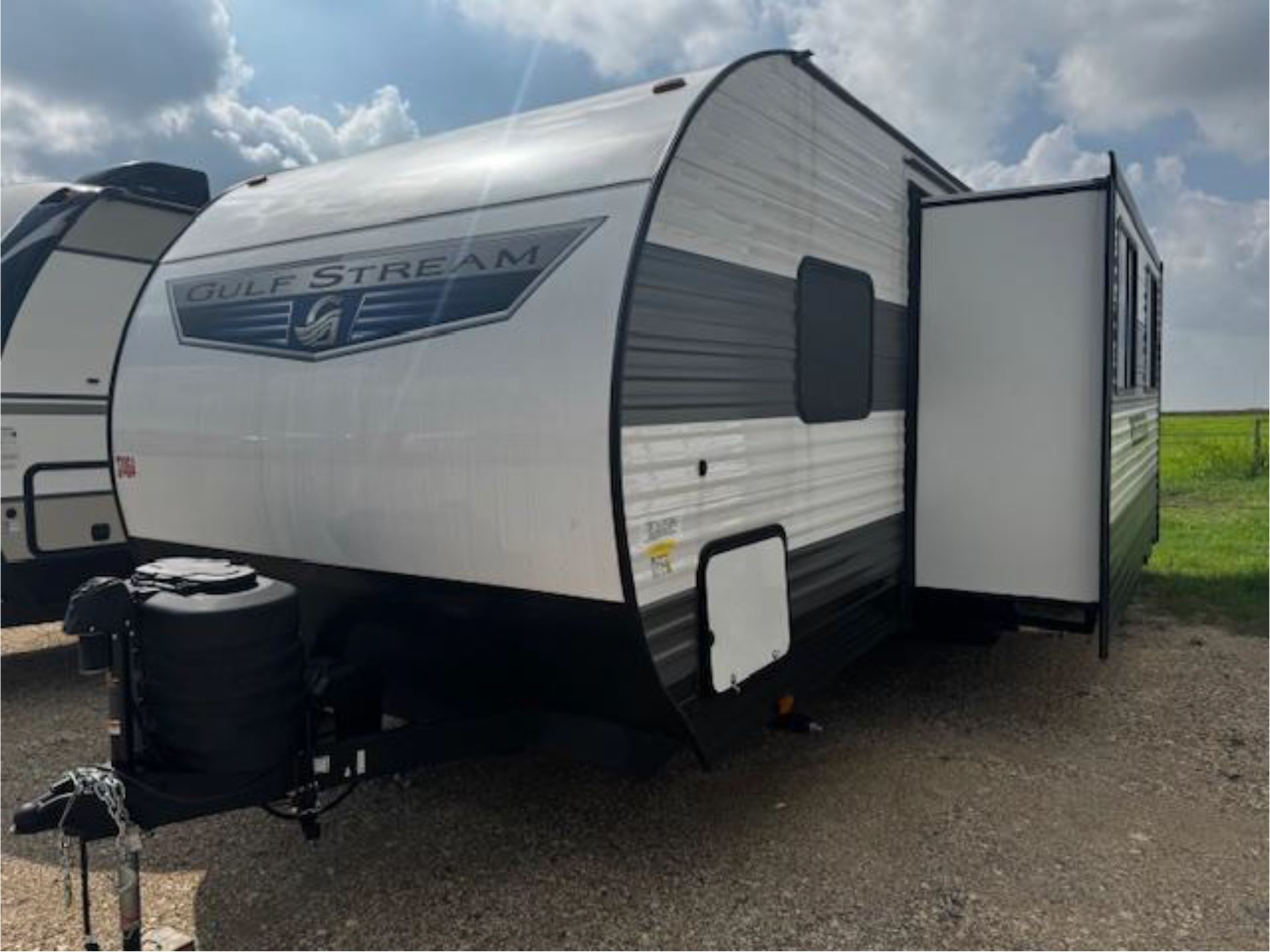 A white and black trailer is parked in a gravel lot