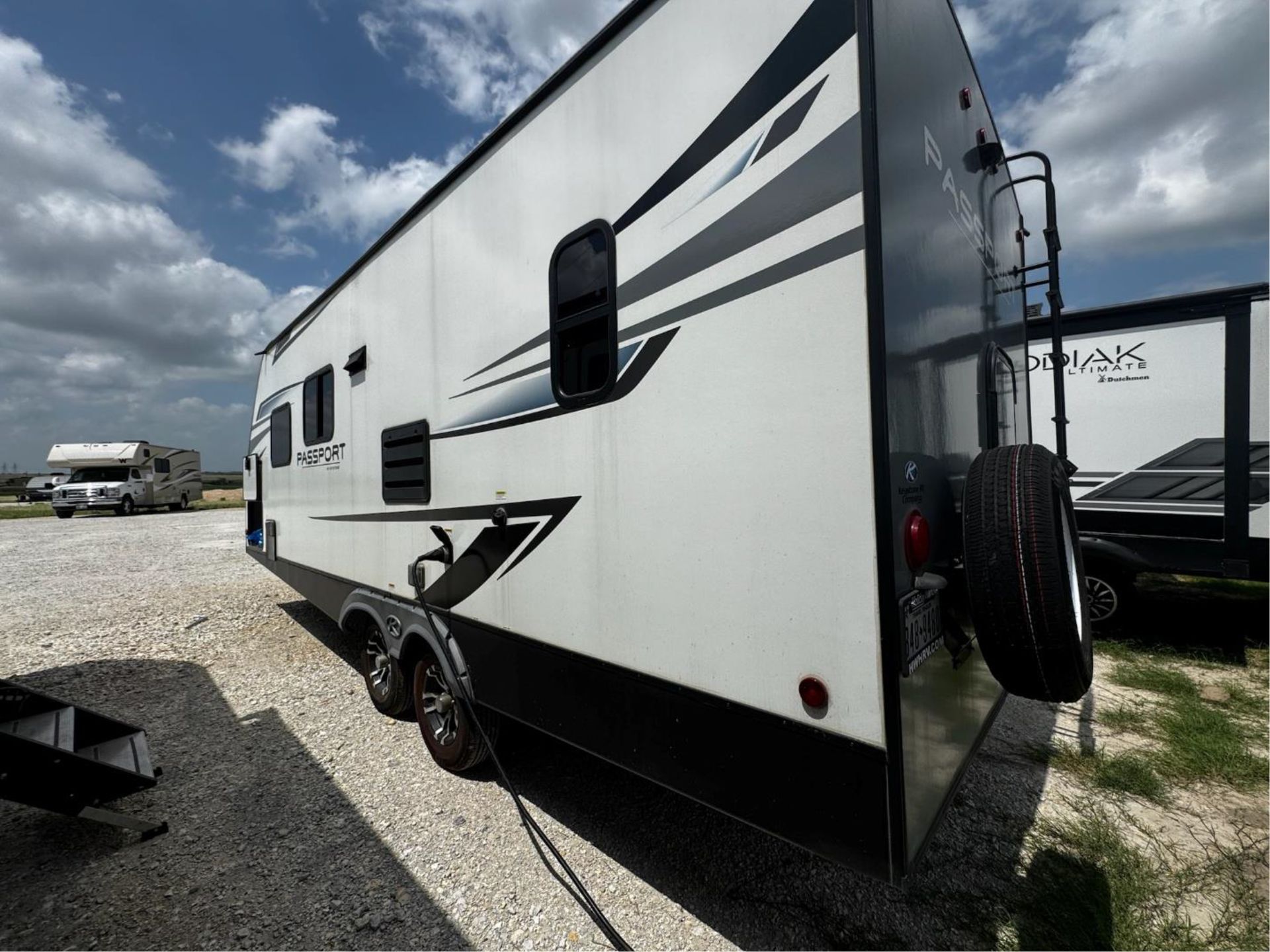 A white and black trailer is parked in a gravel lot