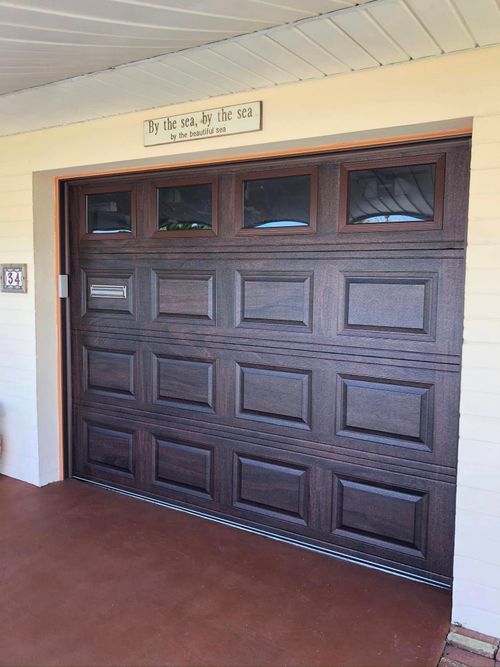 Large dark wooden garage door with small windows in a beige entryway