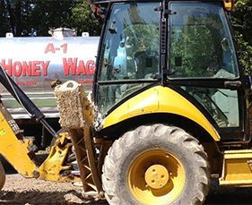 A yellow tractor is parked in front of a tanker that says A-1 honey wagon