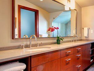 Bathroom with double sinks, cherry cabinets, light countertops, large mirror.