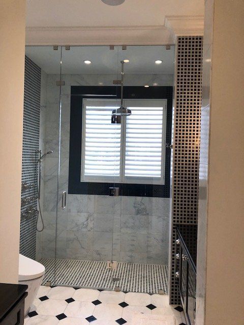 Bathroom with a glass shower, white shutters, and black and white patterned tile flooring.