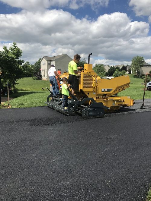 Workers paving a road with a yellow asphalt paver under a cloudy sky