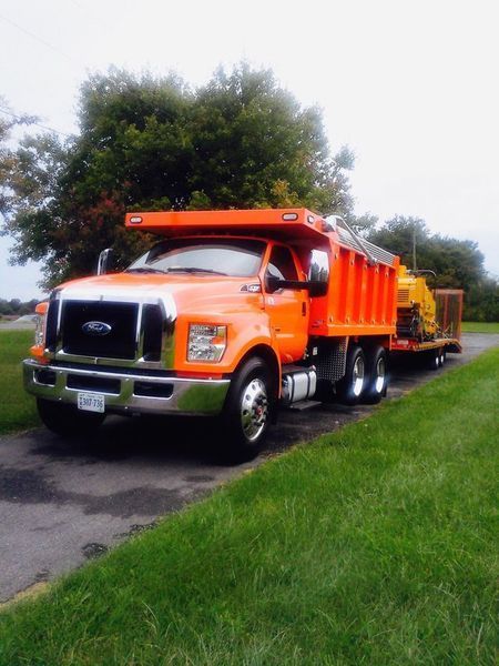 Orange dump truck parked on a driveway beside green grass and trees
