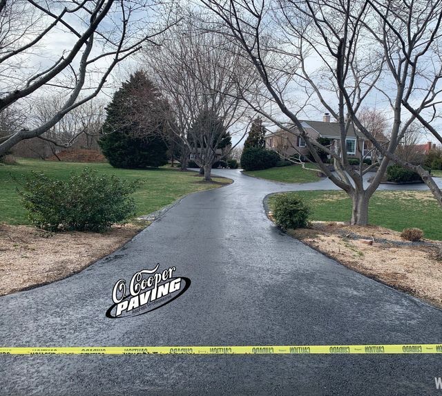 Winding blacktop driveway through a leafless suburban yard, with caution tape across the foreground.