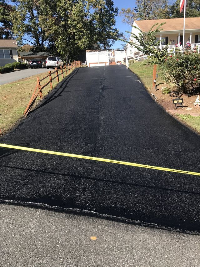Freshly paved black driveway leading to a gated entrance, with a yellow tape across the foreground.