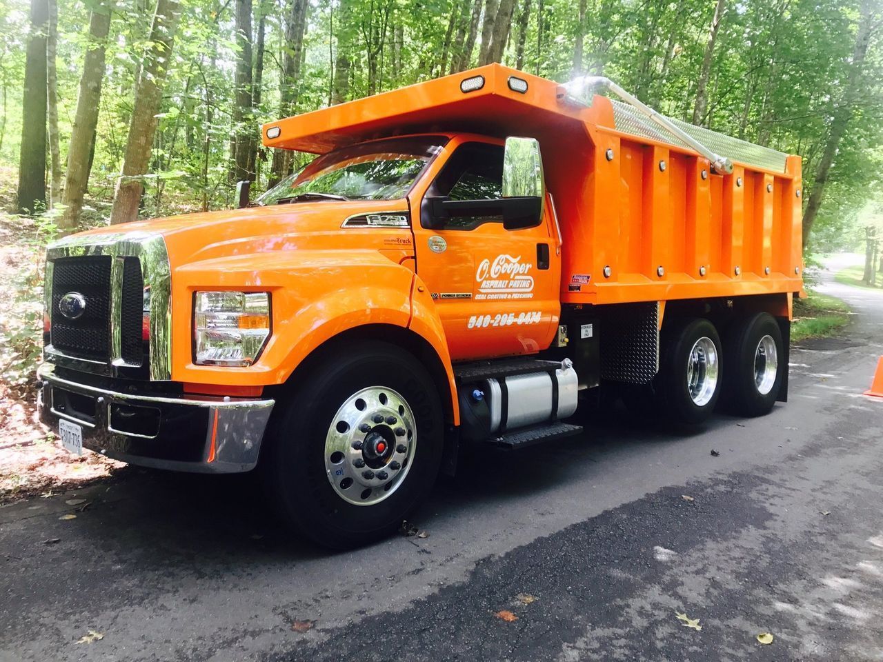 Orange dump truck parked on a forest road, viewed from the front-left side.