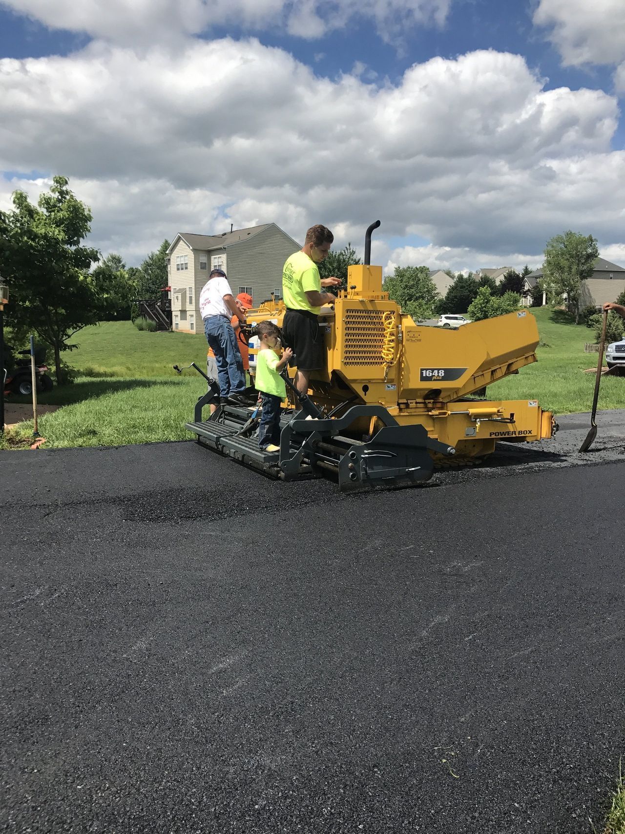 Workers paving a road with a yellow asphalt machine under a cloudy sky