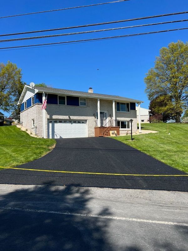 Two-story house with a newly paved black driveway. Blue sky, green grass.