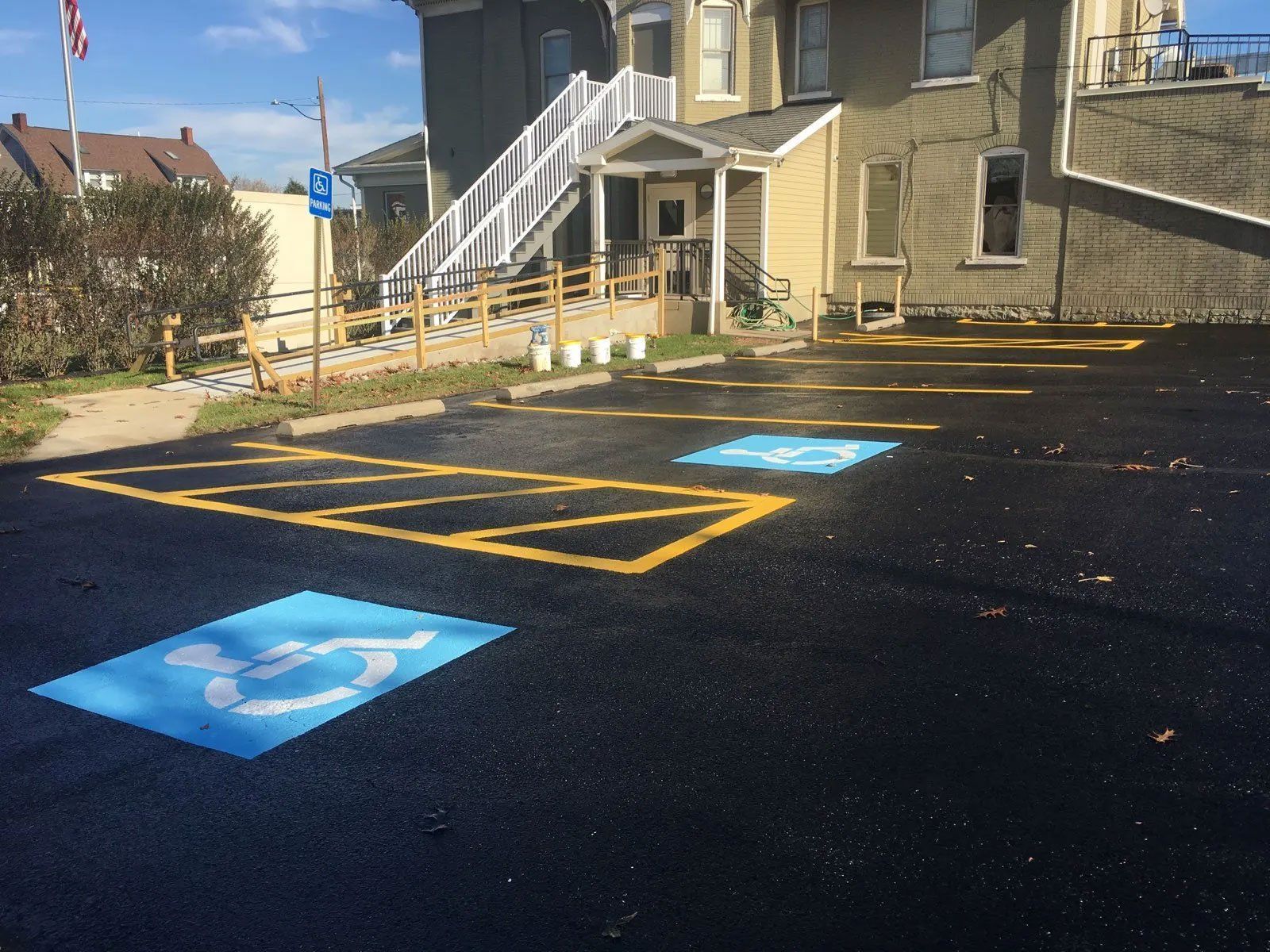Asphalt parking lot with handicap parking spaces marked in blue and yellow near a building with a ramp.