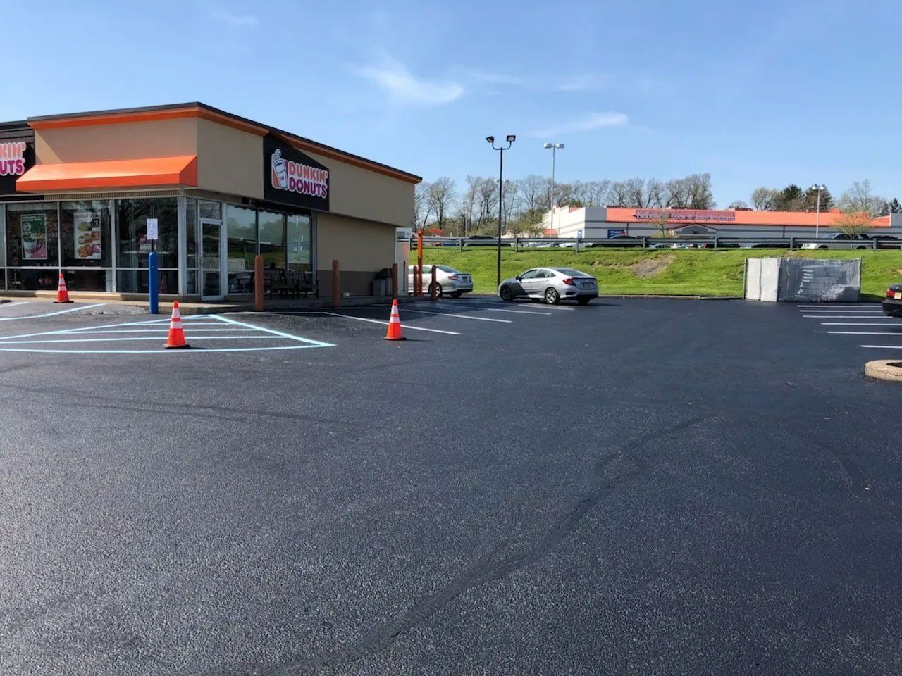 Newly paved Dunkin' Donuts parking lot with painted parking lines and traffic cones, sunny day.