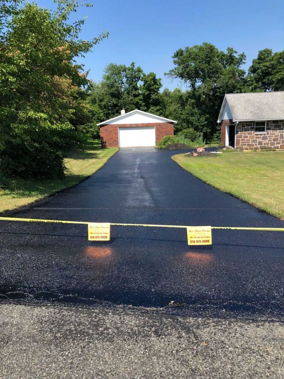 Freshly paved black driveway leads to a garage; yellow caution tape blocks access.