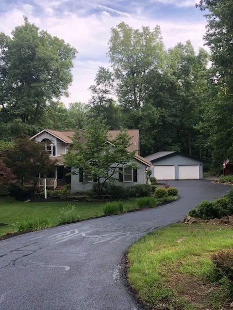 House with light blue siding, two-car garage, and asphalt driveway surrounded by trees and green grass.