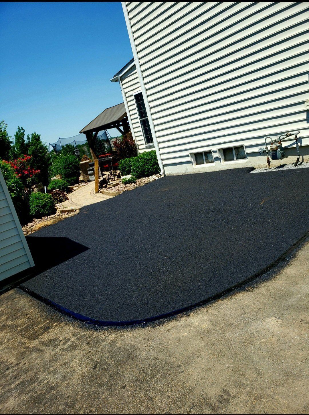 Black rubberized surface next to a house with white siding and blue trim.