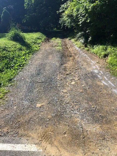 A gravel driveway leading uphill, surrounded by grass and trees.