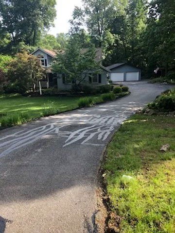 A house with a driveway marked with white lines, surrounded by trees and grass.