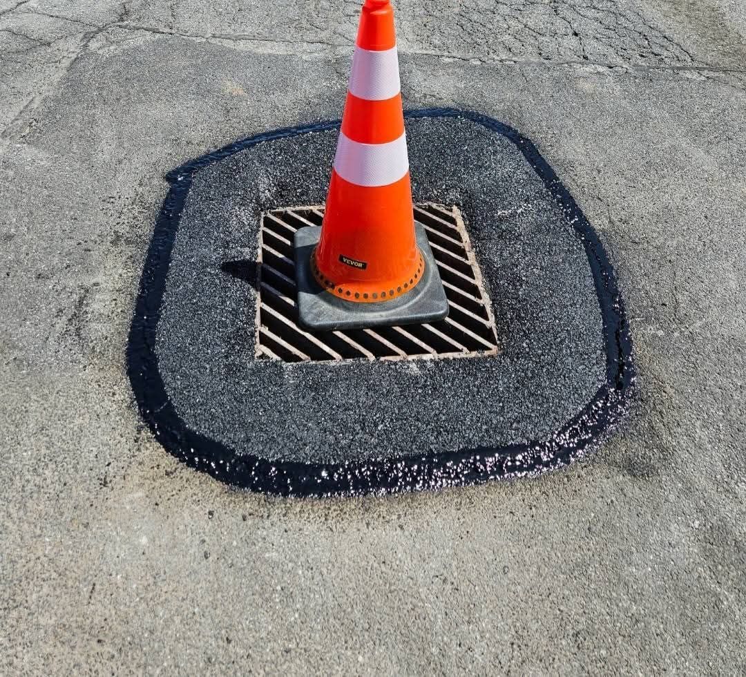 Orange traffic cone on a grated drain in a dark patch of asphalt.