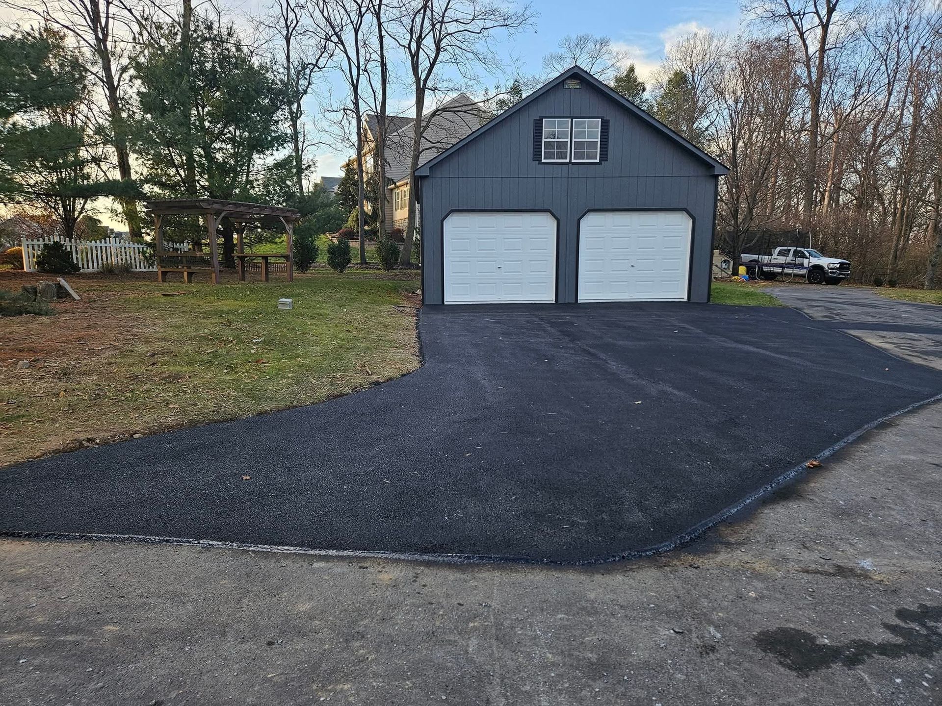 Asphalt driveway leading to a two-car garage with a dark gray exterior and white garage doors.