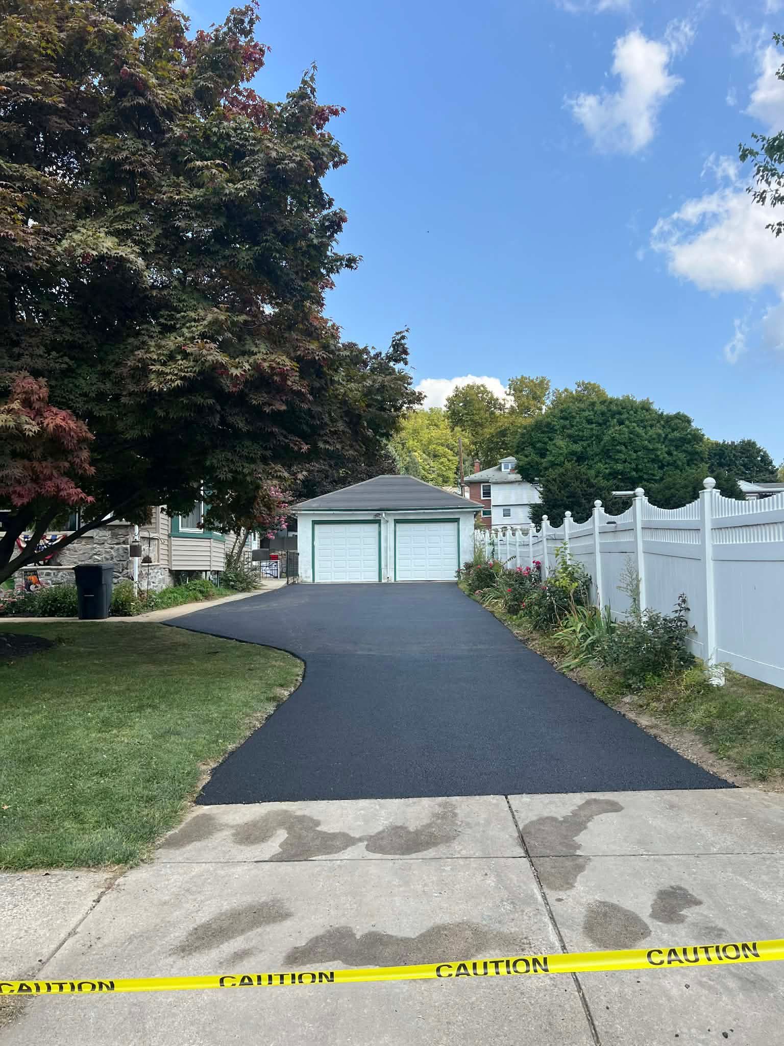 Newly paved asphalt driveway leading to a two-car garage, with caution tape across the concrete entrance.