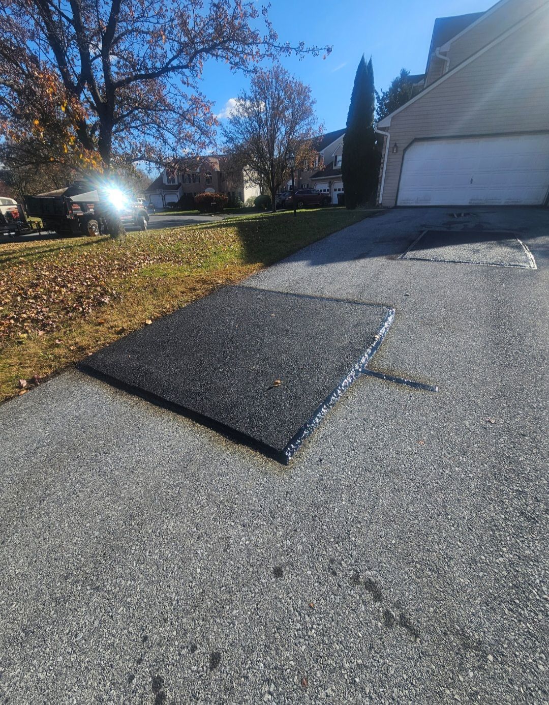 Asphalt patch on a driveway, with a paved road in the foreground and a house in the background.