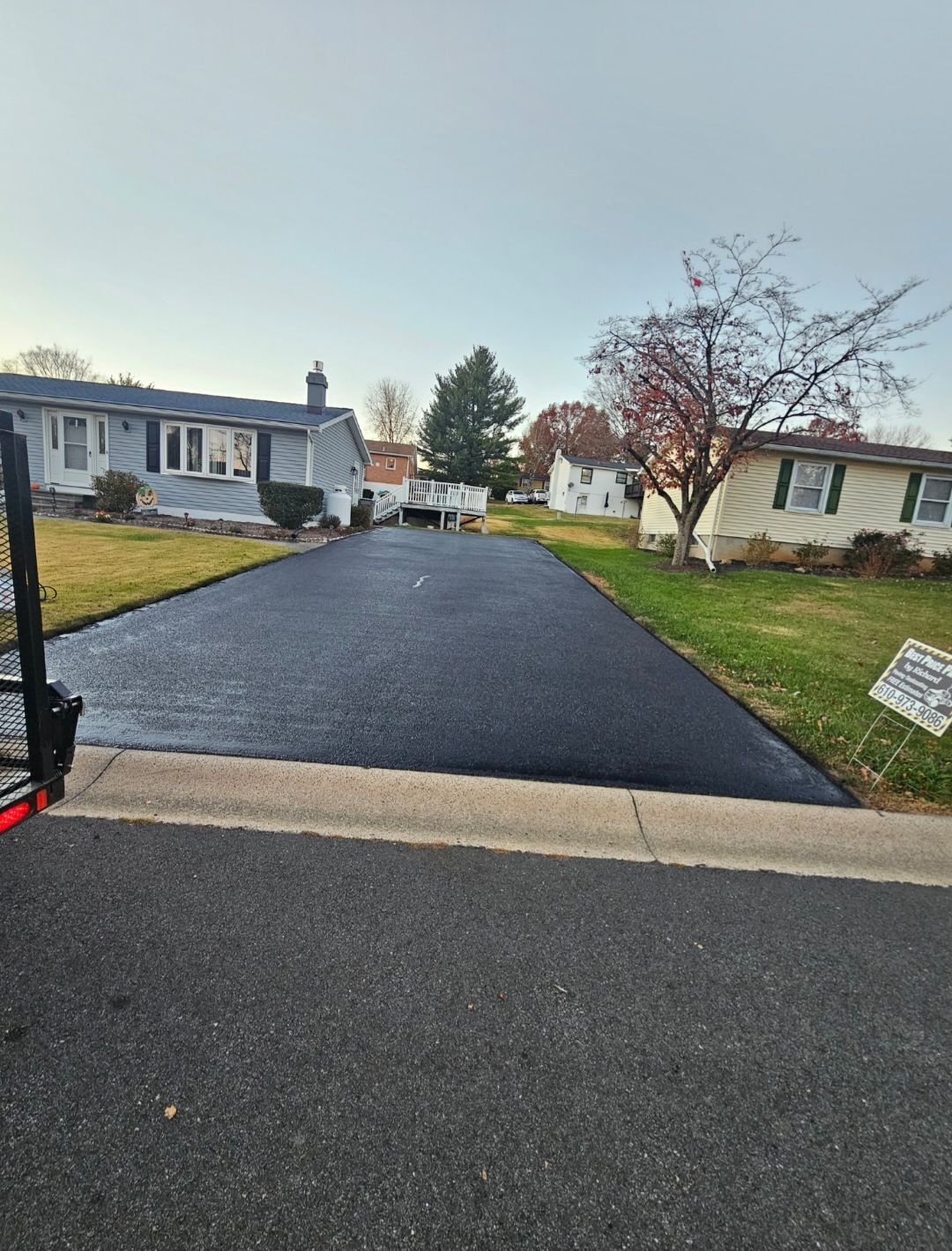 Freshly paved asphalt driveway in front of a house, bordered by curb and grassy lawn.