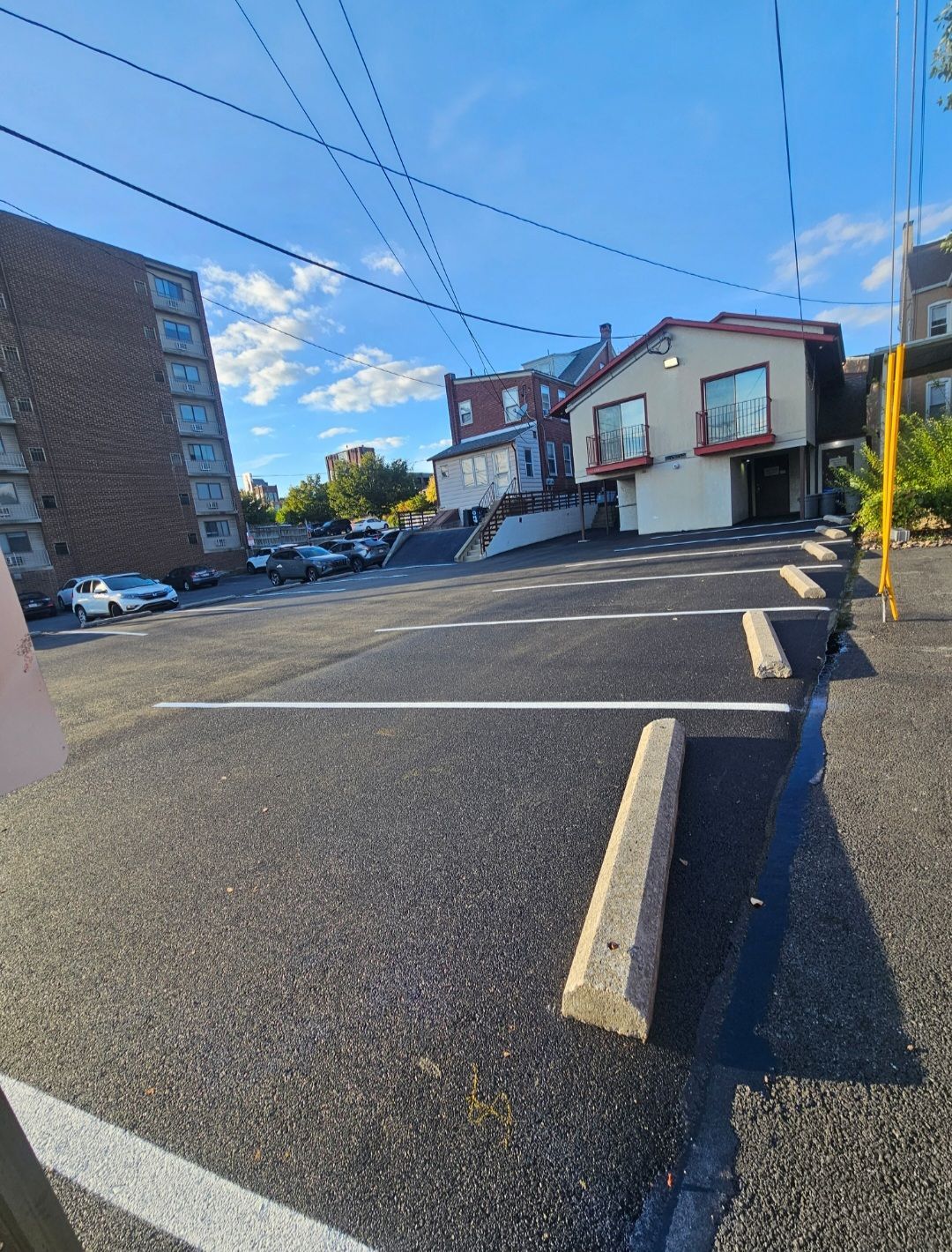 Parking lot with white lines, concrete parking stops, and buildings on a sunny day.