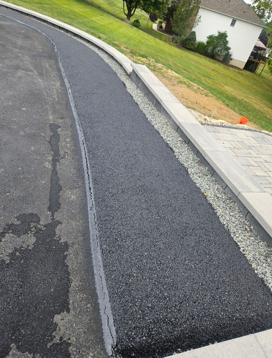 Asphalt driveway with fresh gravel and concrete border, leading to a home on a hillside.