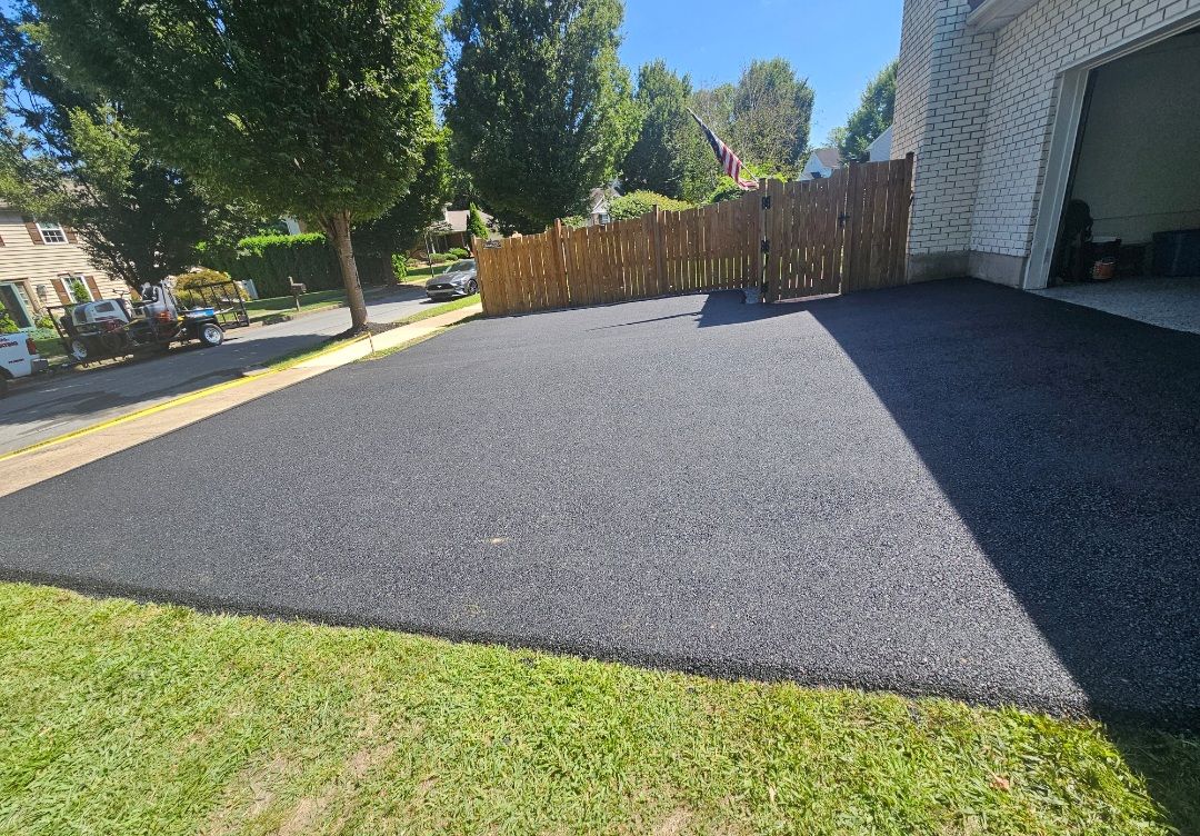 Black asphalt driveway next to green grass and a wooden fence, with a garage on the right.