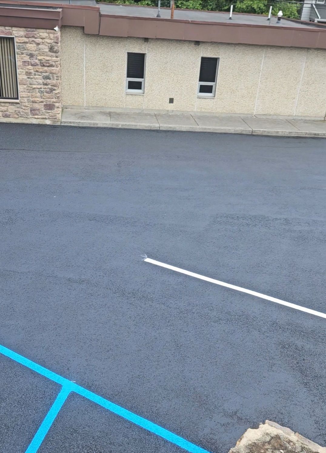 Freshly paved asphalt parking lot with white and blue painted lines, adjacent to a tan building.