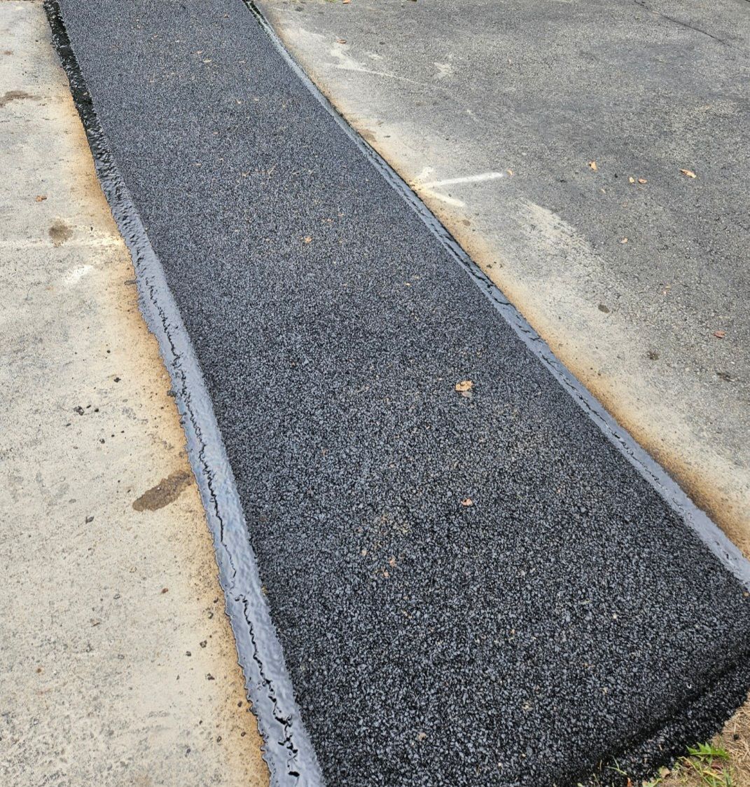 Freshly paved asphalt strip, dark gray, bordered by concrete.