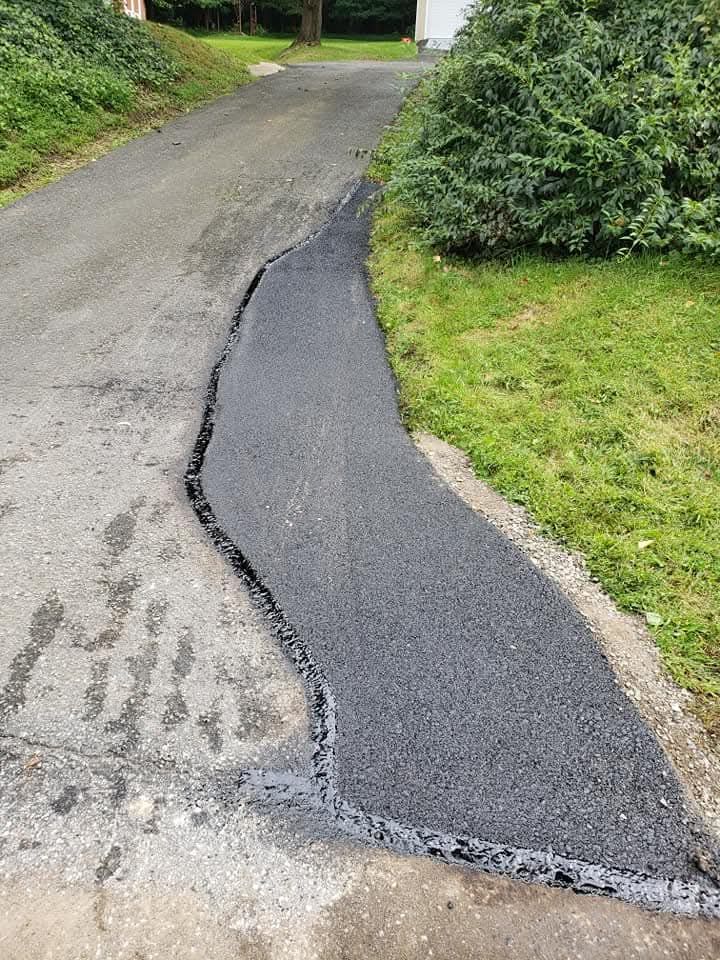 A newly paved strip of asphalt patches the edge of an existing driveway next to a grass lawn.