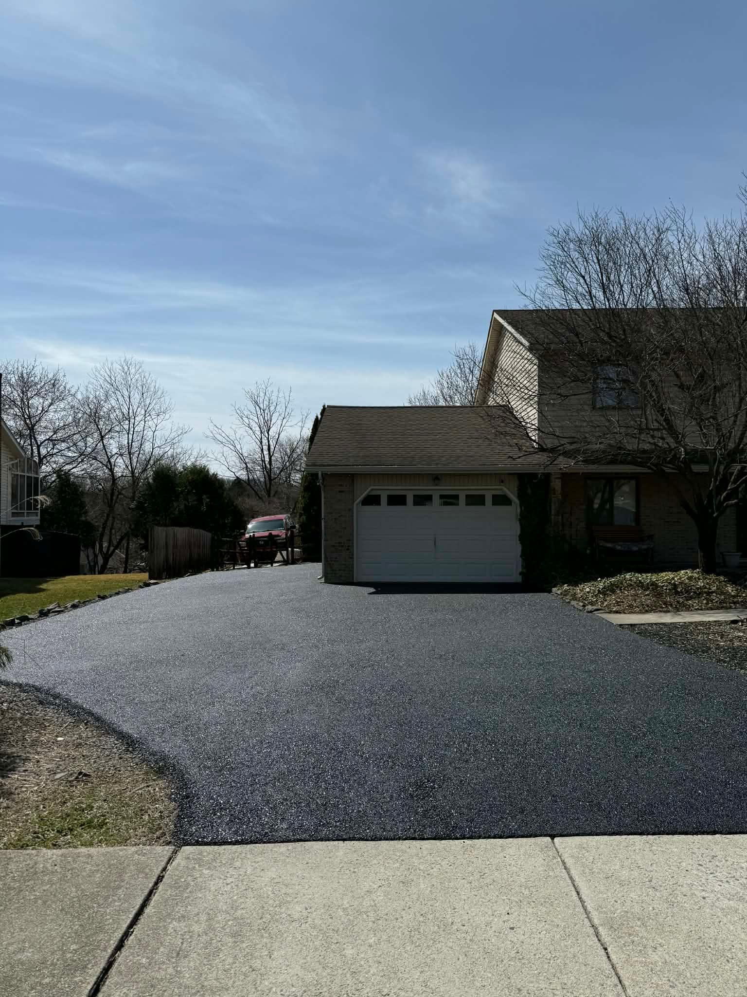 A wide asphalt driveway leads to the garage of a suburban home under a clear blue sky.
