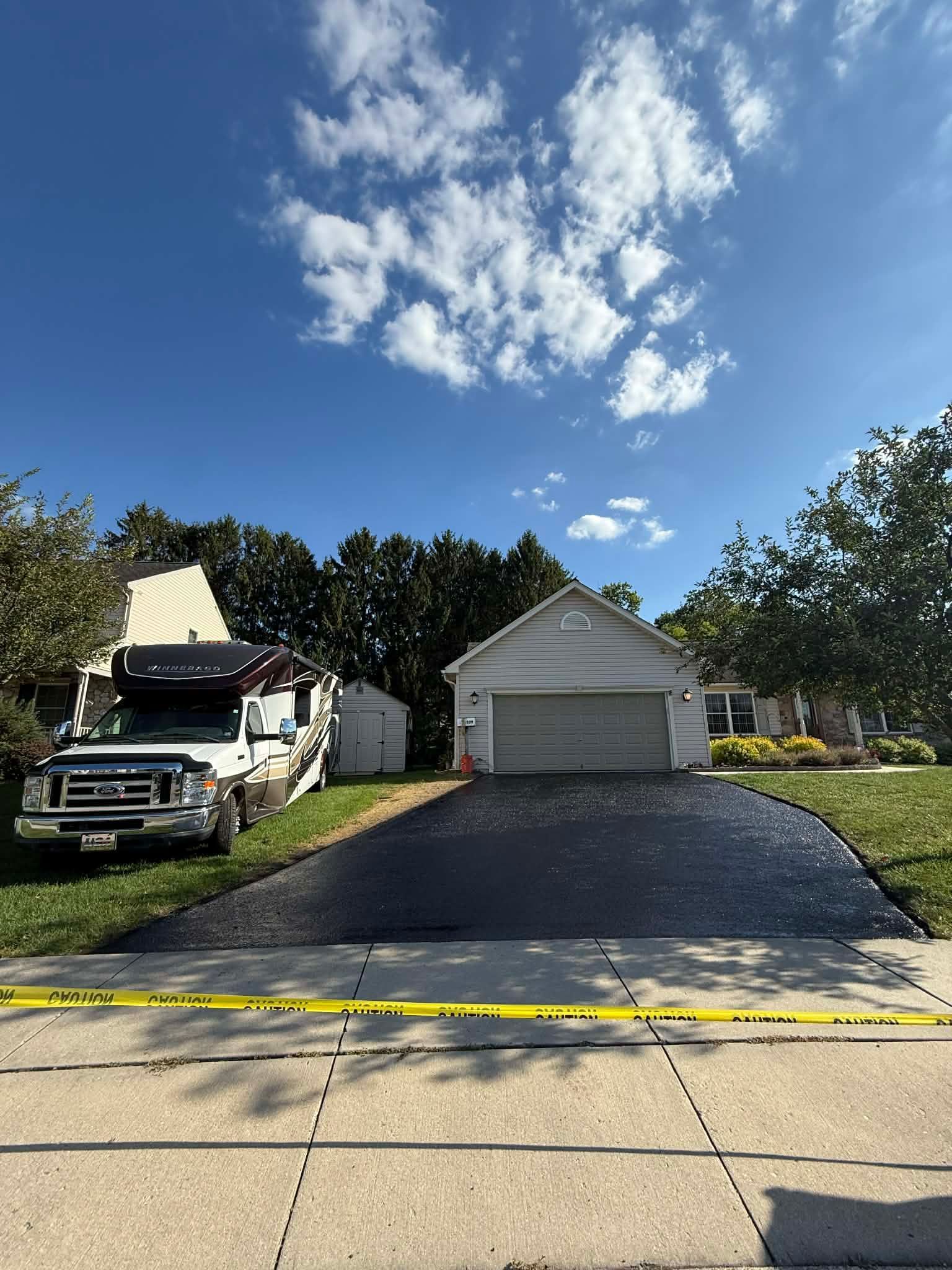 A black truck parked on the grass beside a house with a freshly paved asphalt driveway, fronted by yellow caution tape.