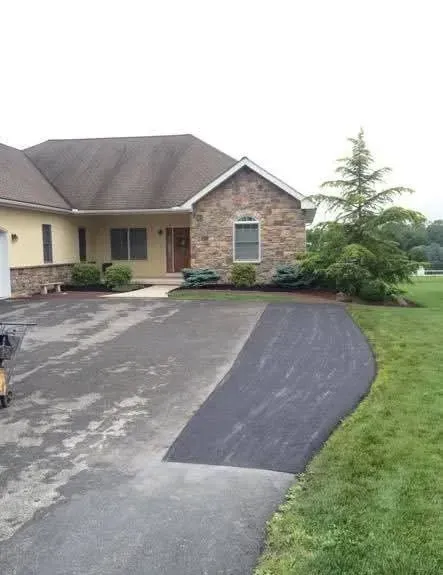 A house with stone and tan siding features a driveway with a recently paved, darker asphalt section on the right side.