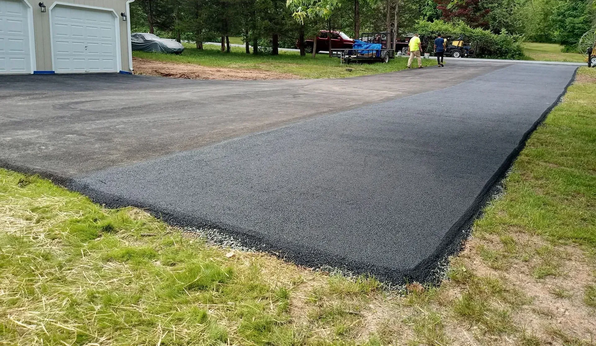 Newly paved, smooth black asphalt driveway leading to a garage in a grassy residential area.