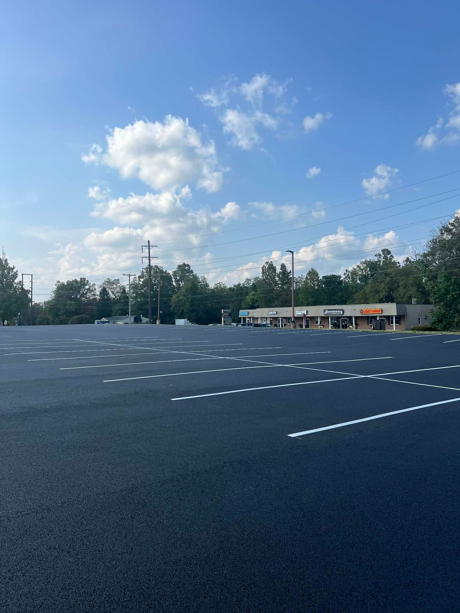 A newly paved parking lot with freshly painted white dashed lines under a bright blue sky with a distant shopping strip.