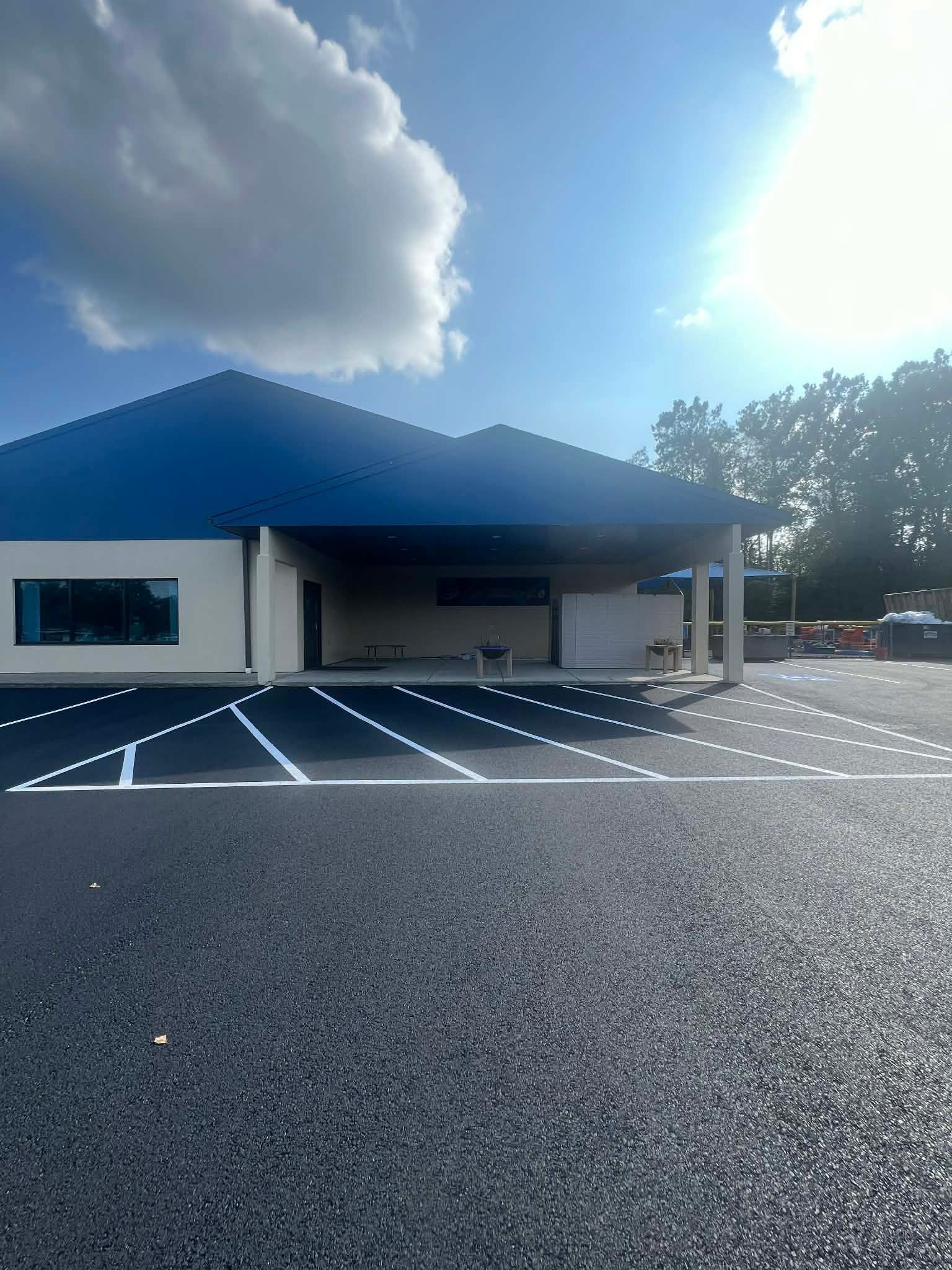 A single-story building with a blue roof, dark exterior, and a freshly paved parking lot with white painted markings.